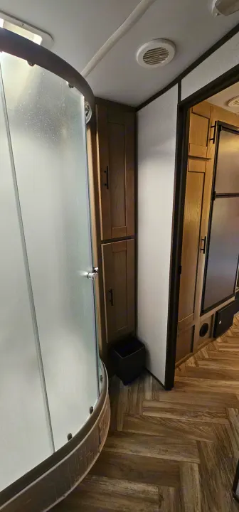 Inside an RV rental: a compact bathroom area with a curved frosted shower, built-in wooden storage, and a view into the main living space.. Cruiser RV Shadow Cruiser 2021