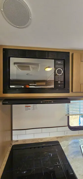 RV rental kitchen featuring a Greystone microwave, range hood, and stovetop, offering a compact cooking area.. Cruiser RV Shadow Cruiser 2021