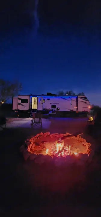 Camping with an RV rental: A warm campfire contrasts with a modern RV's blue lights at dusk.. Cruiser RV Shadow Cruiser 2021