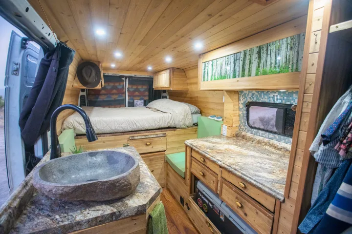 Cozy RV rental interior with custom wood, a bed, stone sink, and granite counter kitchen. Perfect camper van experience.. Dodge Sprinter Van 2016