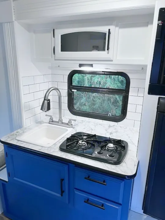 Modern RV kitchen with blue cabinets, white subway tile backsplash, sink, and stove – ideal for an rv rental.. Winnie Drop Winnie Drop Trailer 2017