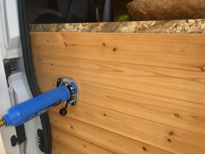 RV rental ready: Blue TastePURE RV water filter mounted on the wooden interior of a camper van.. Dodge Sprinter Van 2016
