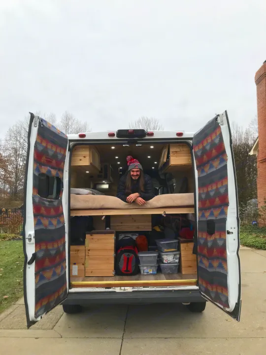 Explore van life! Man smiles from his customized camper van, featuring a bed & storage – great for RV rental.. Dodge Sprinter Van 2016
