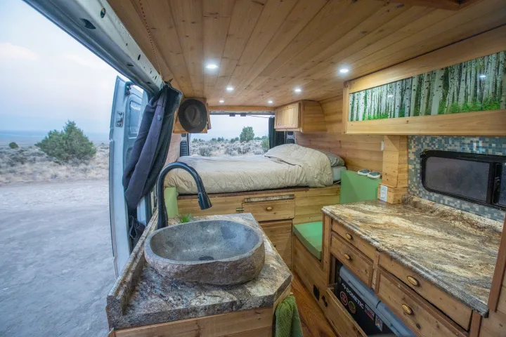 This RV rental's cozy interior boasts a stone sink, full bed, and warm wood finishes, perfect for mobile adventures.. Dodge Sprinter Van 2016