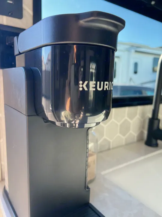 A black Keurig coffee maker sits on a modern RV rental kitchen counter with hexagon tiles. Enjoy coffee on the go!. Jayco 224BHW 2024