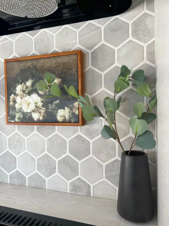 Elegant RV rental kitchen with grey hexagon tile backsplash, framed floral art, and a vase of eucalyptus.. Jayco 224BHW 2024