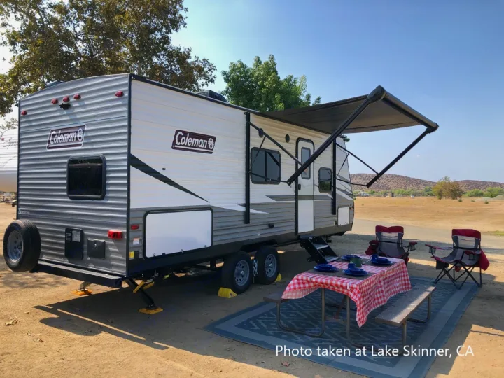 Scenic RV rental setup at Lake Skinner, CA. Coleman travel trailer with awning, picnic table, and chairs for outdoor enjoyment.. Dutchmen Coleman Lantern LT 2021
