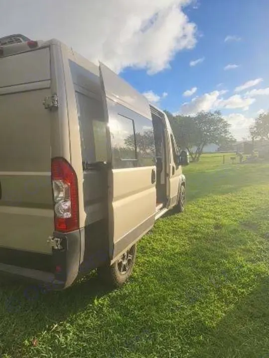 Experience nature with this RV rental camper van, parked on green grass with its side door open under a sunny sky.. Dodge Ram Promaster 2021