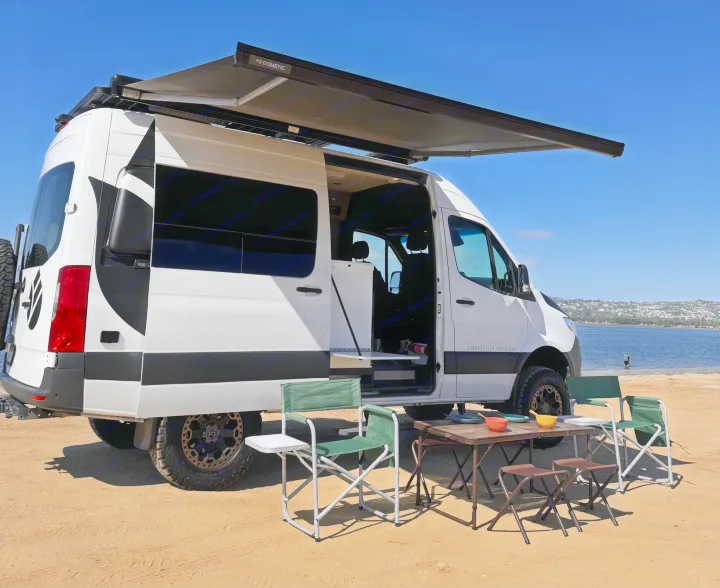 Enjoy the perfect beach day with this RV rental! A Storyteller Overland camper van with a Dometic awning set up on sand by water.. Storyteller Overland Storyteller Overland Class B 2020