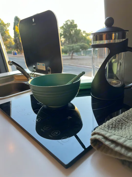 RV rental kitchen setup, featuring an induction cooktop, French press, and a bowl with a spoon, bathed in morning light.. Storyteller Overland Storyteller Overland Class B 2020