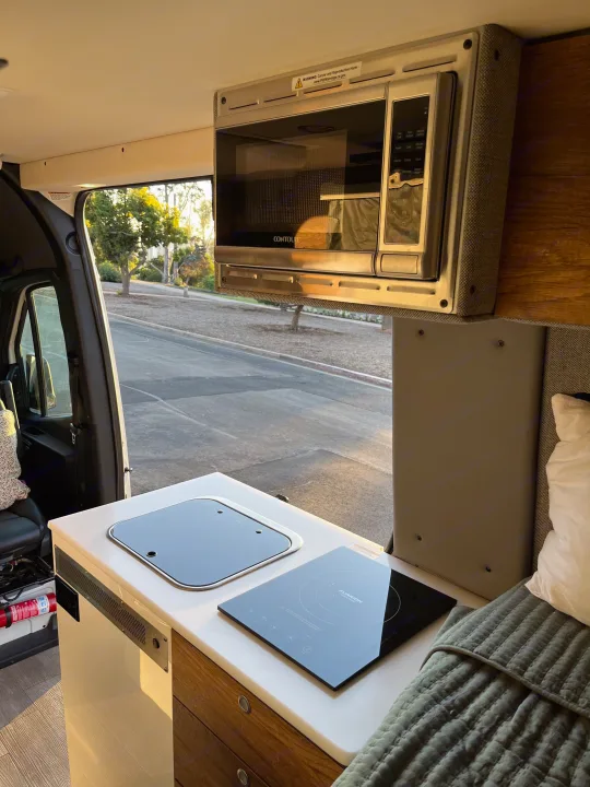 Inside an RV rental: a compact kitchen featuring a microwave, sink, and induction cooktop for mobile living.. Storyteller Overland Storyteller Overland Class B 2020