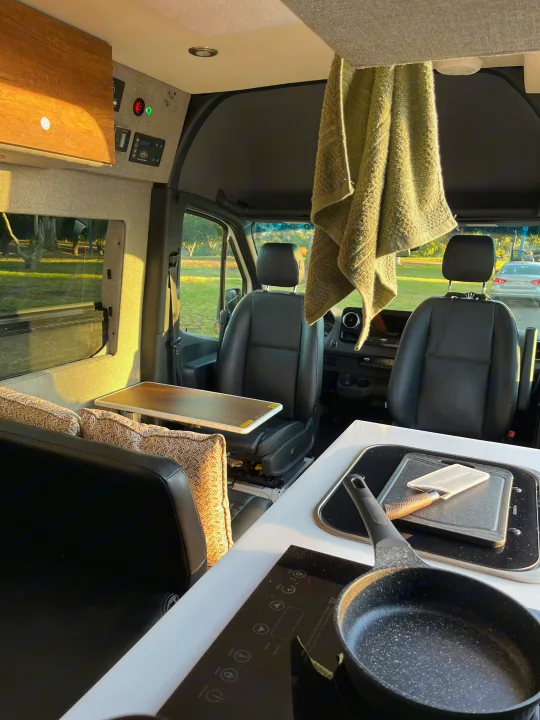 Spacious RV rental interior: front cockpit, side seating with table, and kitchen with induction cooktop. Perfect camper van living.. Storyteller Overland Storyteller Overland Class B 2020