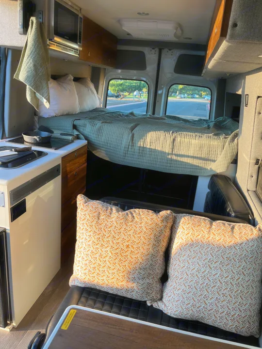 Inside an rv rental: comfortable bed, kitchen with microwave, and patterned pillows on a bench for a homey travel experience.. Storyteller Overland Storyteller Overland Class B 2020