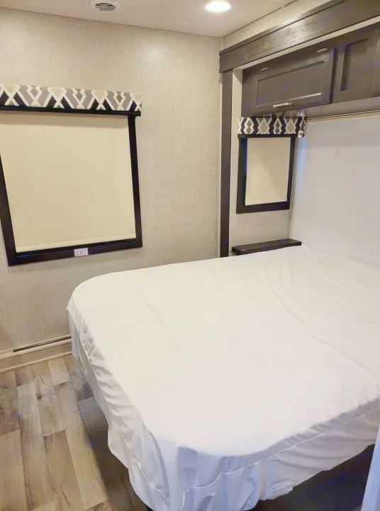 Clean and inviting RV rental bedroom with a large bed, windows, overhead cabinets, and wood-look flooring.. Jayco Greyhawk 2022