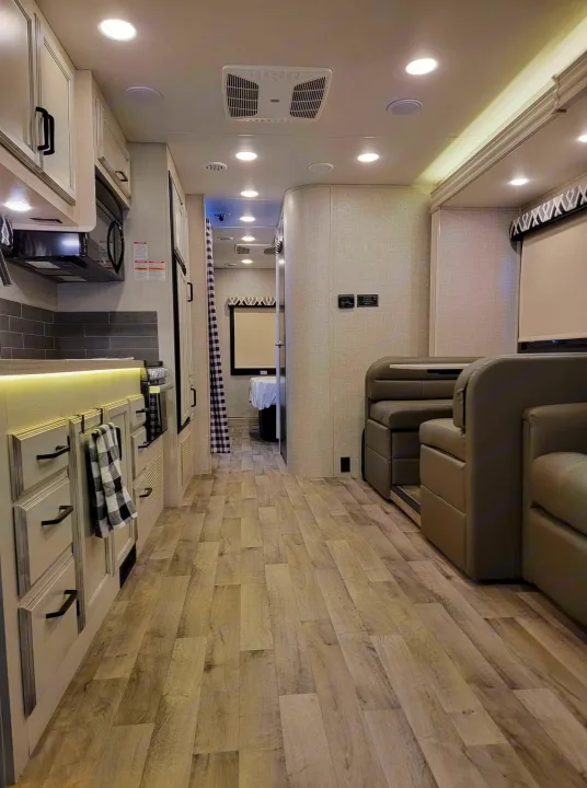 Modern RV rental interior featuring a well-lit kitchen, comfortable seating, and a hallway view leading to the bedroom.. Jayco Greyhawk 2022