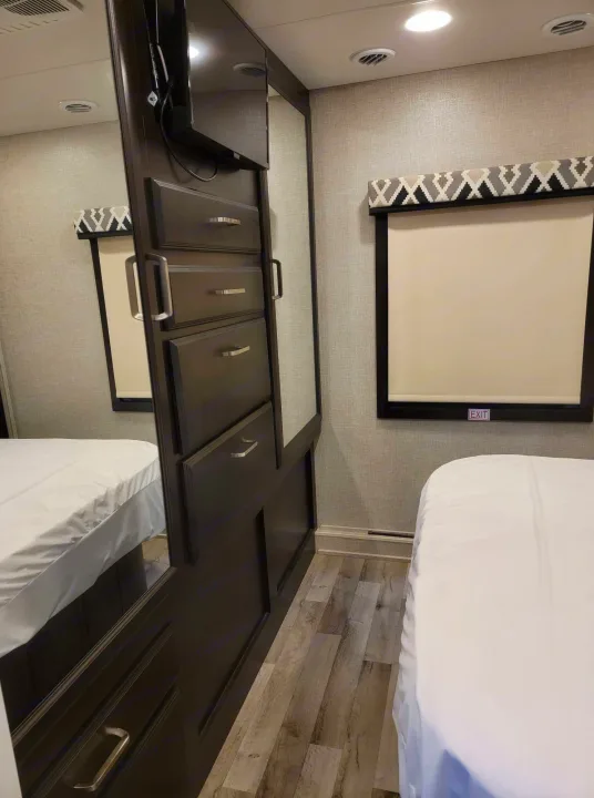 Inside a modern RV rental bedroom with a comfy bed, dark wood wardrobe & mounted TV, and a window with a stylish valance.. Jayco Greyhawk 2022