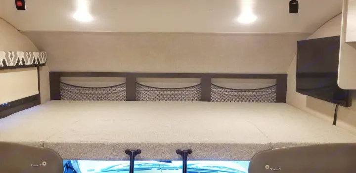 Spacious RV rental cab-over bunk with mesh storage, TV, window shade, and comfortable sleeping area.. Jayco Greyhawk 2022