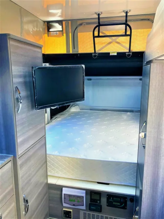 Interior of an RV rental showing a compact bedroom with a bed, wall-mounted TV, cabinets, & control panels.. OBI OBI Popup Trailer 2022