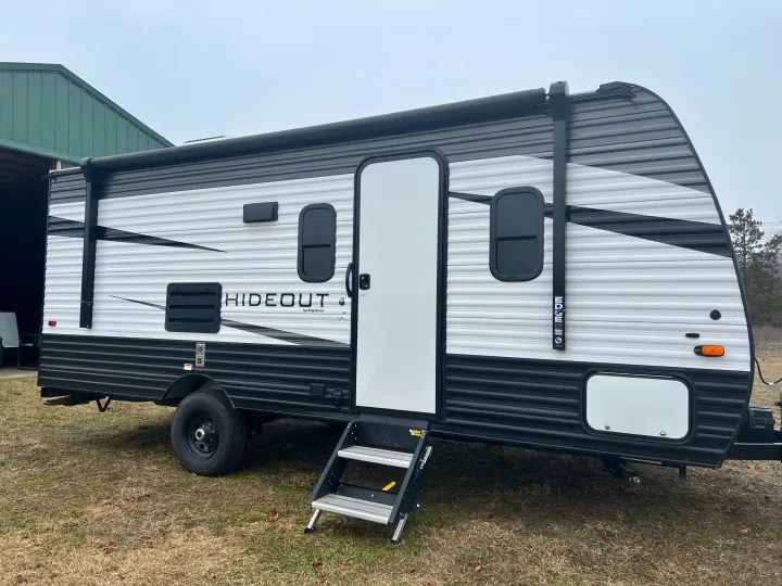 Side view of a white and black Hideout travel trailer RV rental with its door open and steps extended, parked on a grassy area.. Keystone RV Hideout 2021