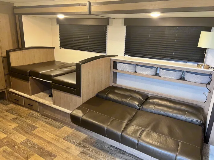 Cozy RV rental interior with a convertible dinette bed, brown leather sofa, and practical storage shelving. Ready for your next trip.. Keystone RV Hideout 2021