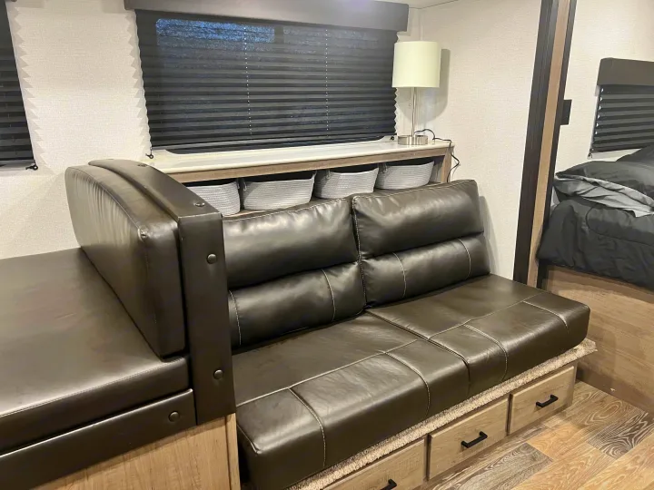 Spacious RV rental interior: L-shaped leather seating with storage drawers, lamp, and blinds for a comfy stay.. Keystone RV Hideout 2021