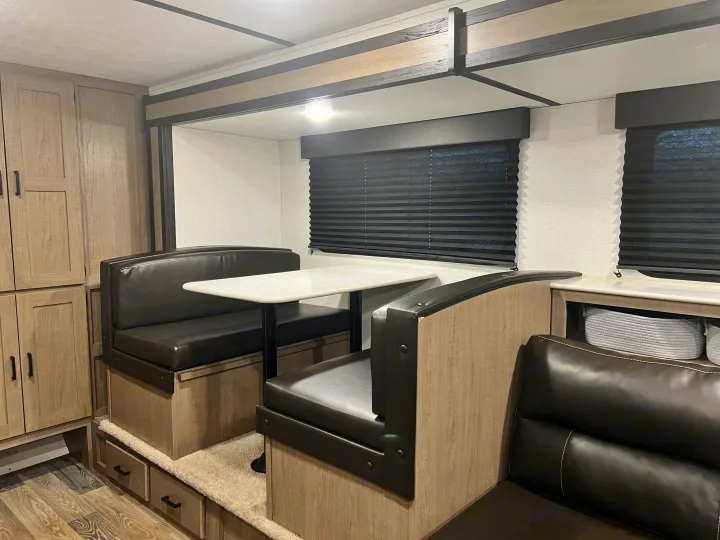 Cozy RV rental dinette with black benches, white table, and light wood cabinetry, perfect for meals and relaxing.. Keystone RV Hideout 2021