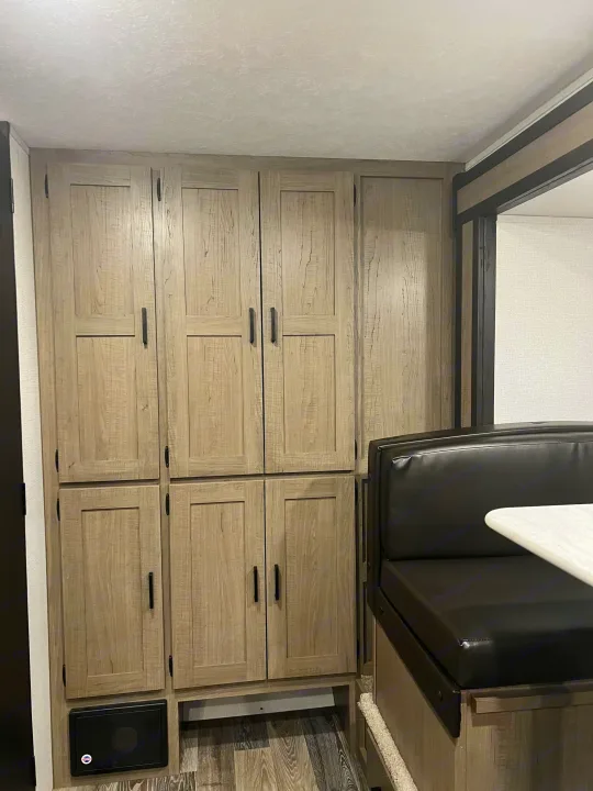 RV rental interior featuring light wood cabinets, a comfy black dinette, and a white table for meals and relaxation.. Keystone RV Hideout 2021
