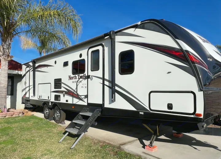 White North Trail Ultralite RV rental parked by a house with palm trees under a blue sky, ready for adventure.. Heartland RVs North Trail 2018