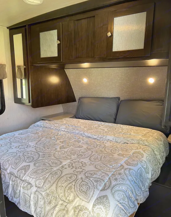 Comfortable RV rental bedroom with a grey paisley comforter, dark cabinets, and integrated reading lights. A cozy travel space.. Heartland RVs North Trail 2018