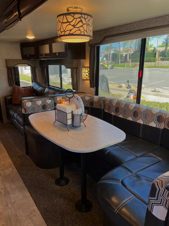 Comfortable RV rental dinette with black seating, patterned cushions, and a white table set for meals, overlooking an outdoor scene.. Heartland RVs North Trail 2018