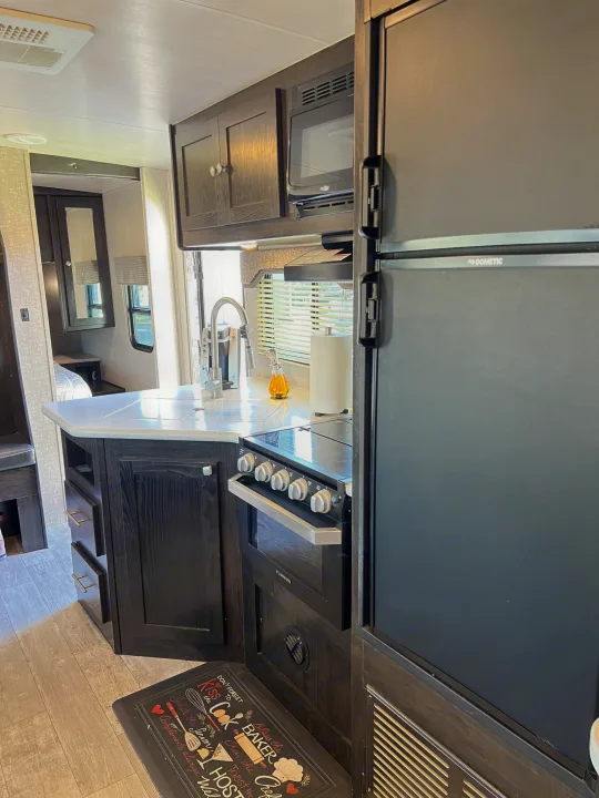 Cozy RV rental kitchen with dark wood cabinets, Dometic fridge, Furrion oven/microwave, and a well-equipped countertop.. Heartland RVs North Trail 2018