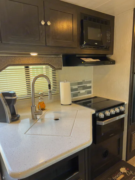Experience comfort in this RV rental's well-equipped kitchen. Features light countertops, dark cabinets, microwave, sink, and oven.. Heartland RVs North Trail 2018