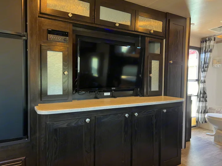 RV rental: Sleek dark wood entertainment center features TV, stereo, and ample storage. Fridge left, bathroom right.. Heartland RVs North Trail 2018