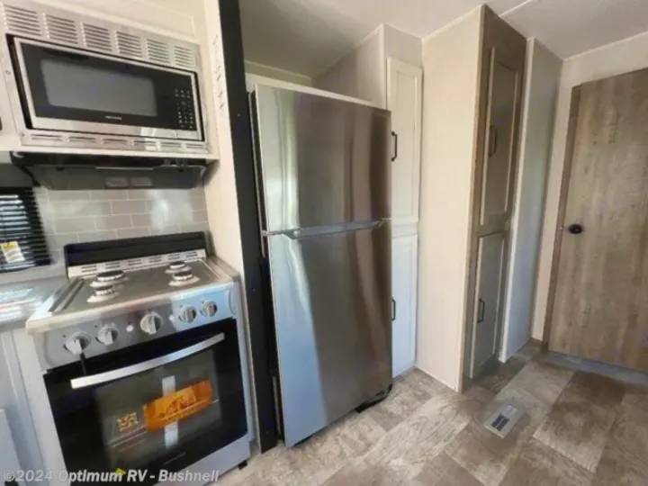 RV rental kitchen featuring stainless steel microwave, range, & large fridge. Compact design with wood-look flooring.. Forest River Palomino Puma 2022