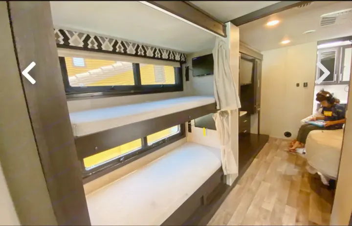 Inside an RV rental, featuring bunk beds with comfortable mattresses, a TV, and a person enjoying quiet time.. Jayco Precept 2021