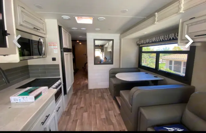 Modern RV rental interior: kitchen with microwave/stove, dining booth, and sofa seating for comfort.. Jayco Precept 2021