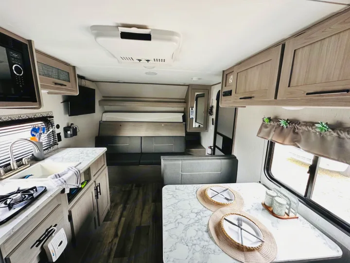 Side of a white and gray Coleman RV rental, featuring windows and the brand logo. Ready for travel!. Dutchmen Coleman Lantern LT 2022
