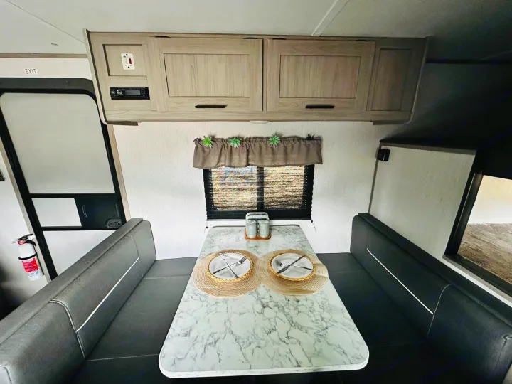A bright RV rental interior featuring a dinette with a marble-top table, black benches, and overhead storage cabinets.. Dutchmen Coleman Lantern LT 2022
