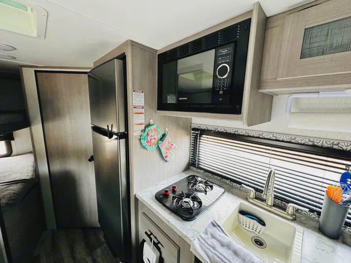 Compact RV rental kitchen featuring a stainless steel fridge, microwave, stove, and sink. Ready for your next adventure!. Dutchmen Coleman Lantern LT 2022