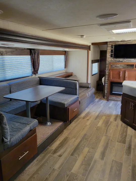 Bright RV rental interior showing a grey dinette, lounge, and fireplace. Wood-style flooring offers a modern feel.. Forest River Cherokee Grey Wolf 2019