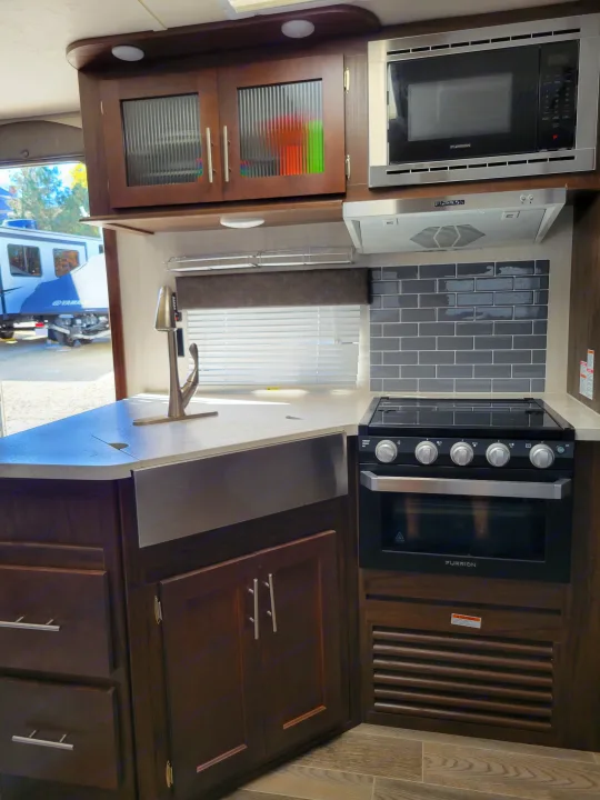 Explore this modern rv rental kitchen, featuring dark wood cabinets, a farmhouse sink, light counters, microwave, and oven.. Forest River Cherokee Grey Wolf 2019