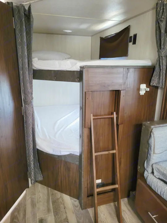 RV rental: This image showcases a compact bunk bed setup inside an RV, complete with white bedding, pillows, and a wooden access ladder, offering a cozy sleeping area.. Forest River Cherokee Grey Wolf 2019