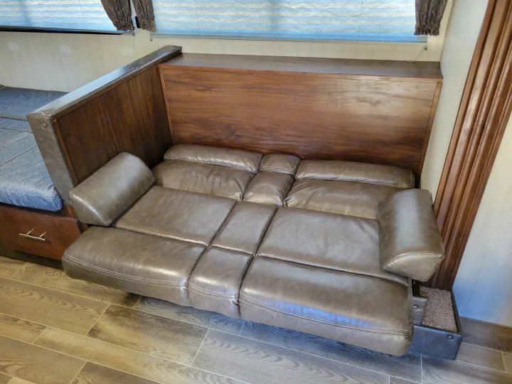 Extended reclinable sofa inside an RV rental, featuring gray faux leather and wood accents for a comfy mobile living space.. Forest River Cherokee Grey Wolf 2019