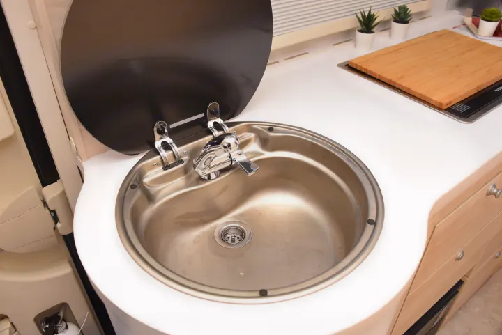 Bright RV rental kitchen featuring a stainless steel sink with open cover, faucet, and a wooden cutting board on the counter.. Nucamp Tab 400 2024