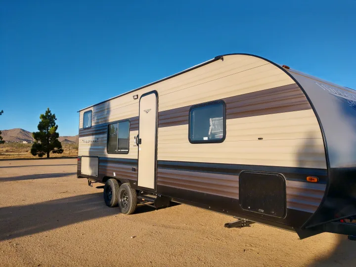 Experience freedom with this large RV rental, a beige & brown travel trailer on a desert lot under a clear blue sky.. Forest River Wildwood 2019