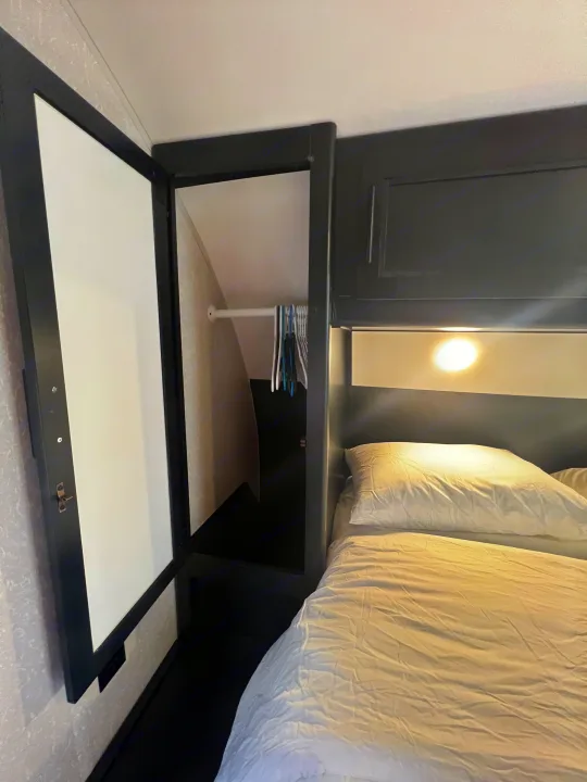 RV rental bedroom: open closet with clothes rod/hangers, plus a comfortable bed with a bright reading light.. Forest River Cherokee 2022