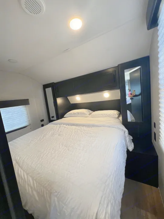 Modern RV rental bedroom featuring a large white bed, sleek black storage, and ambient lighting.. Forest River Cherokee 2022