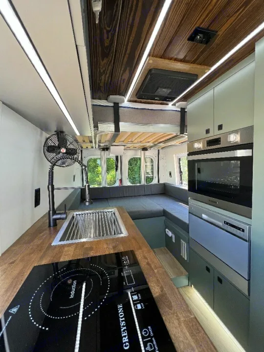 Inside this modern RV rental: a compact kitchen with induction cooktop, sink & appliances. Versatile interior with bed and seating.. 27North 27North Class B 2023
