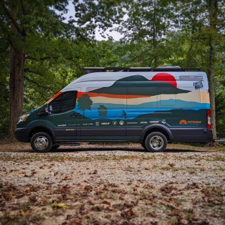 This vibrant RV rental van, custom-painted with mountain and forest art, is ready for adventure on a wooded trail.. Ford Transit 350 HD XLT 2019