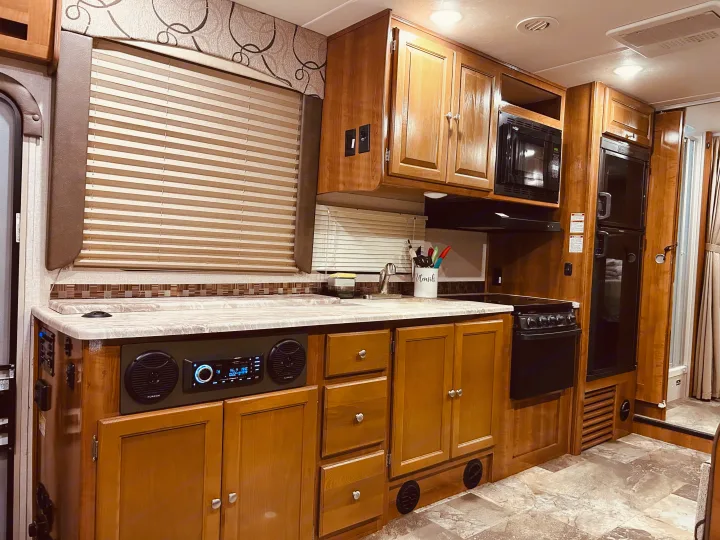 This inviting rv rental interior features a full kitchen with light wood cabinets, appliances, sink, and an entertainment system.. COACHMEN LEPRECHAUN 2019